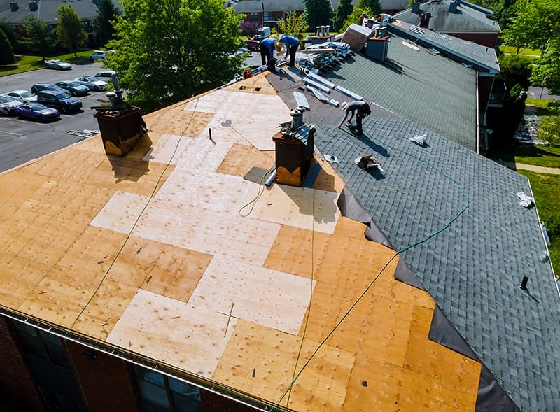 Workers replacing shingles on roof